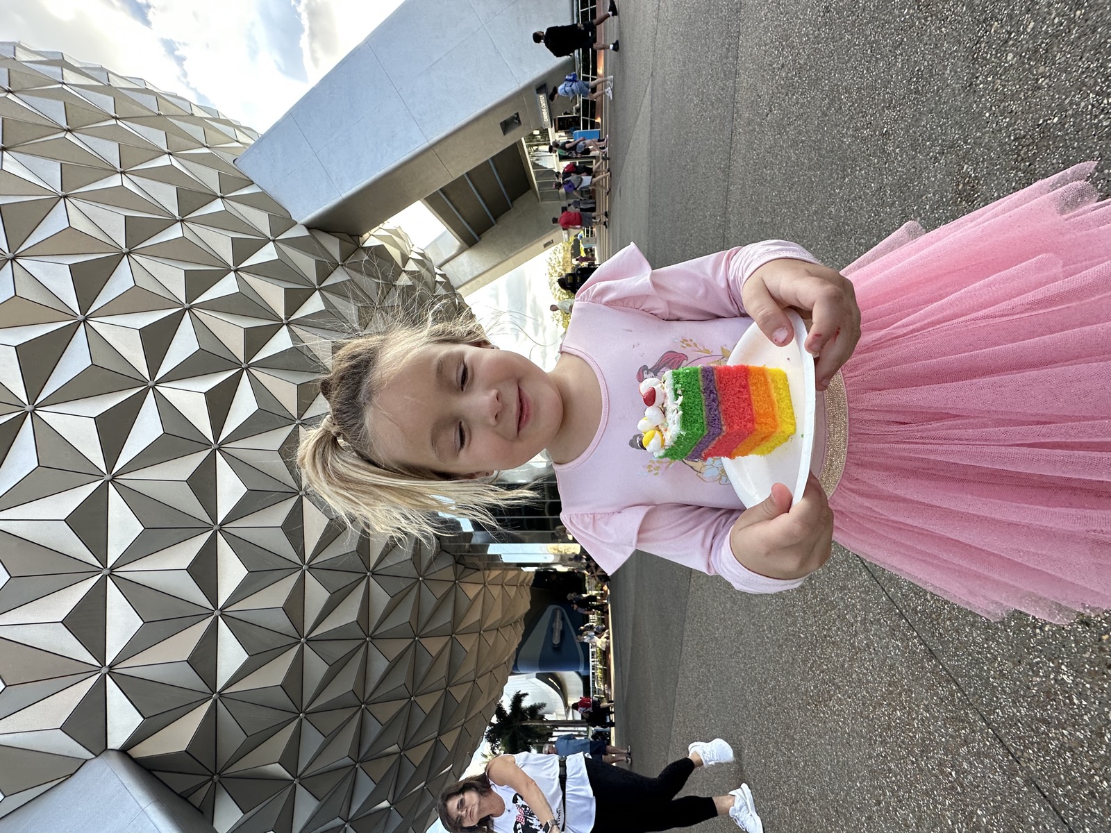 A kid in a princess dress smiling on a sunlit park day.